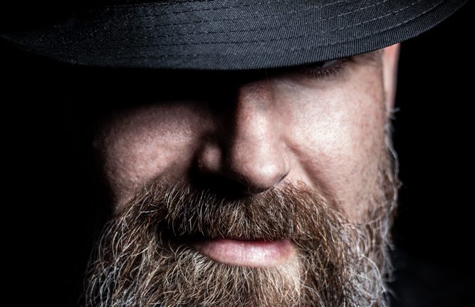 Portraitfotografie Mann mit Bart und Hut lächelt leicht
