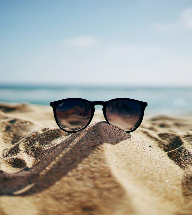 Urlaub Sonnenbrille liegt im Sand am Strand mit Meer im Hintergrund.