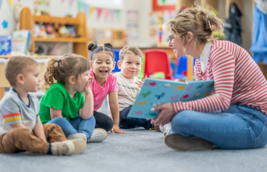 Kita- und Schulfotografie Kinder und Erzieherin sitzen auf dem Boden und lesen eine Geschichte