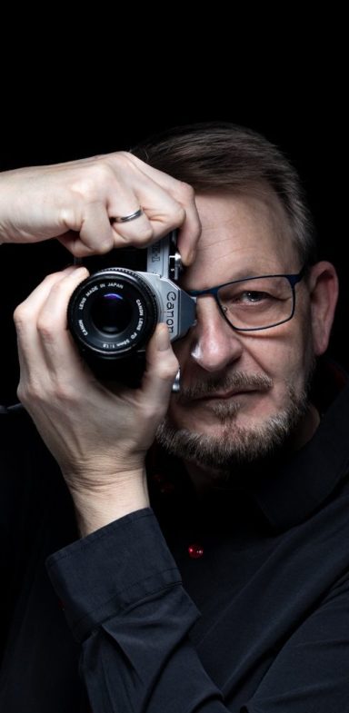 Tim mit Kamera Mann mit Brille hält eine Kamera und schaut durch den Sucher.